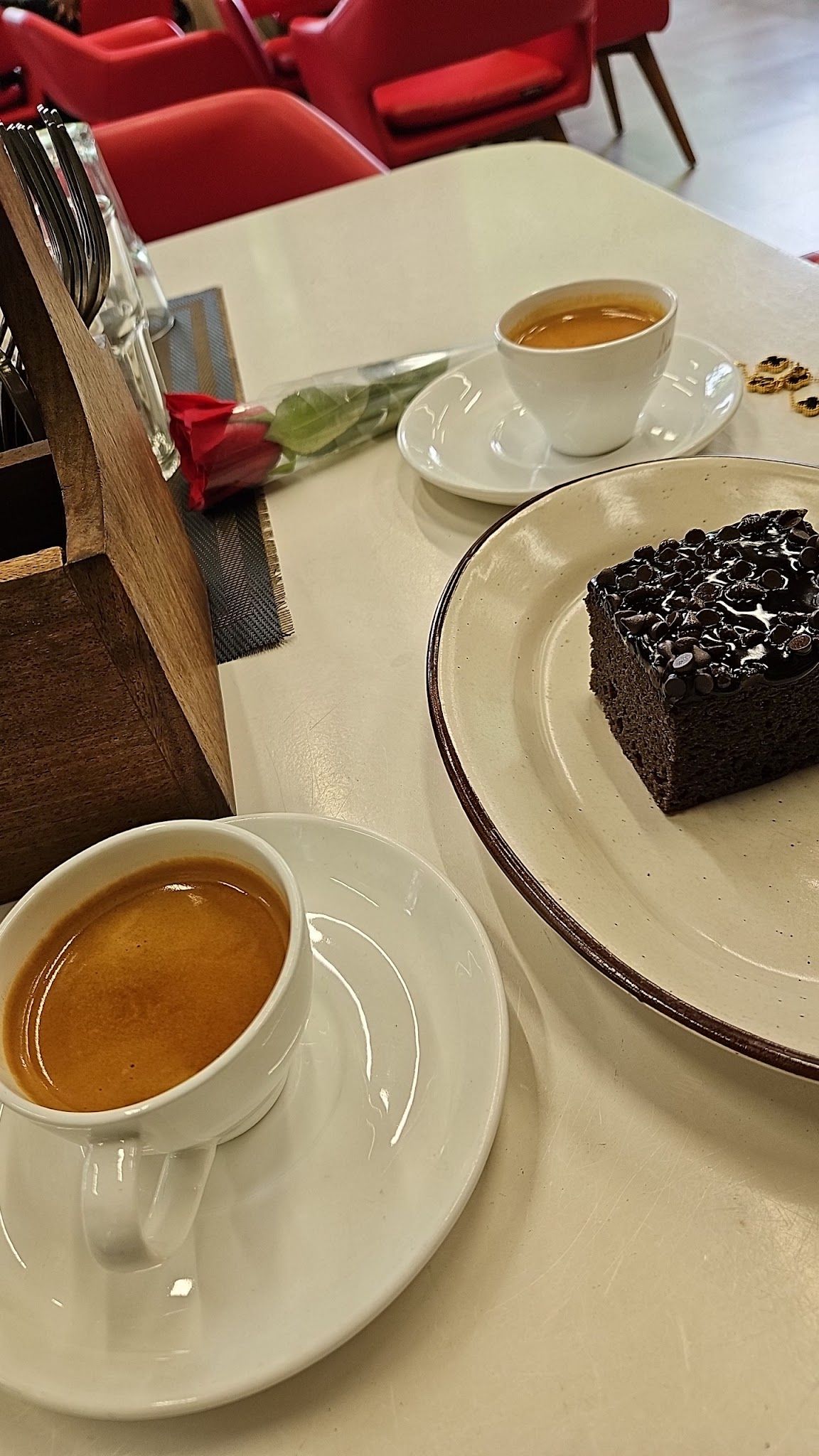 Two espressos and a slice of chocolate cake on a white café table