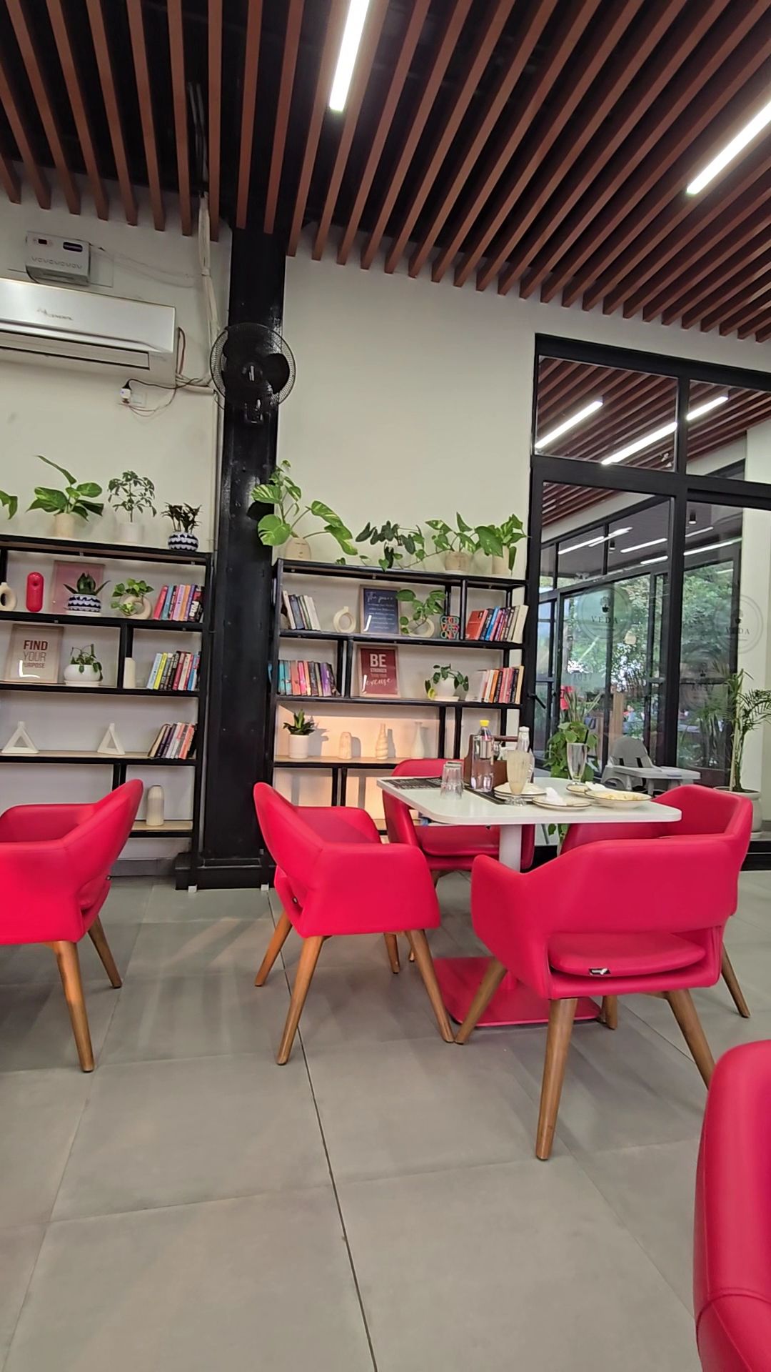 Bookshelves, plants and red chairs inside Veda