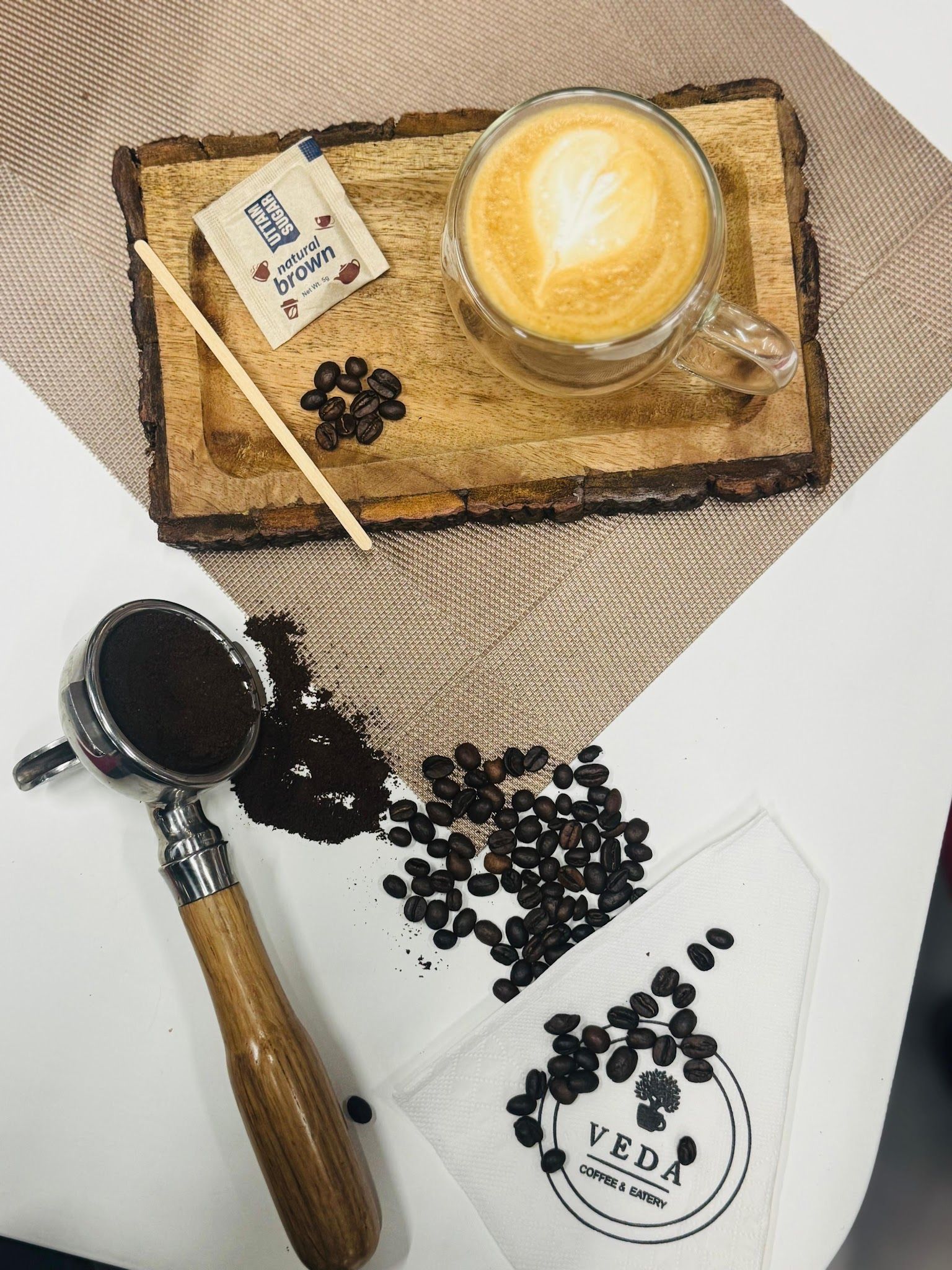 Latte with latte art on a wooden tray with coffee beans and a portafilter