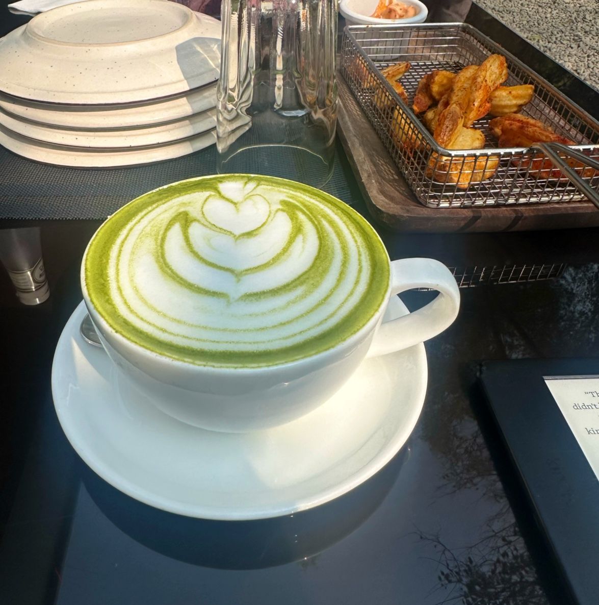A matcha latte with latte art next to potato wedges