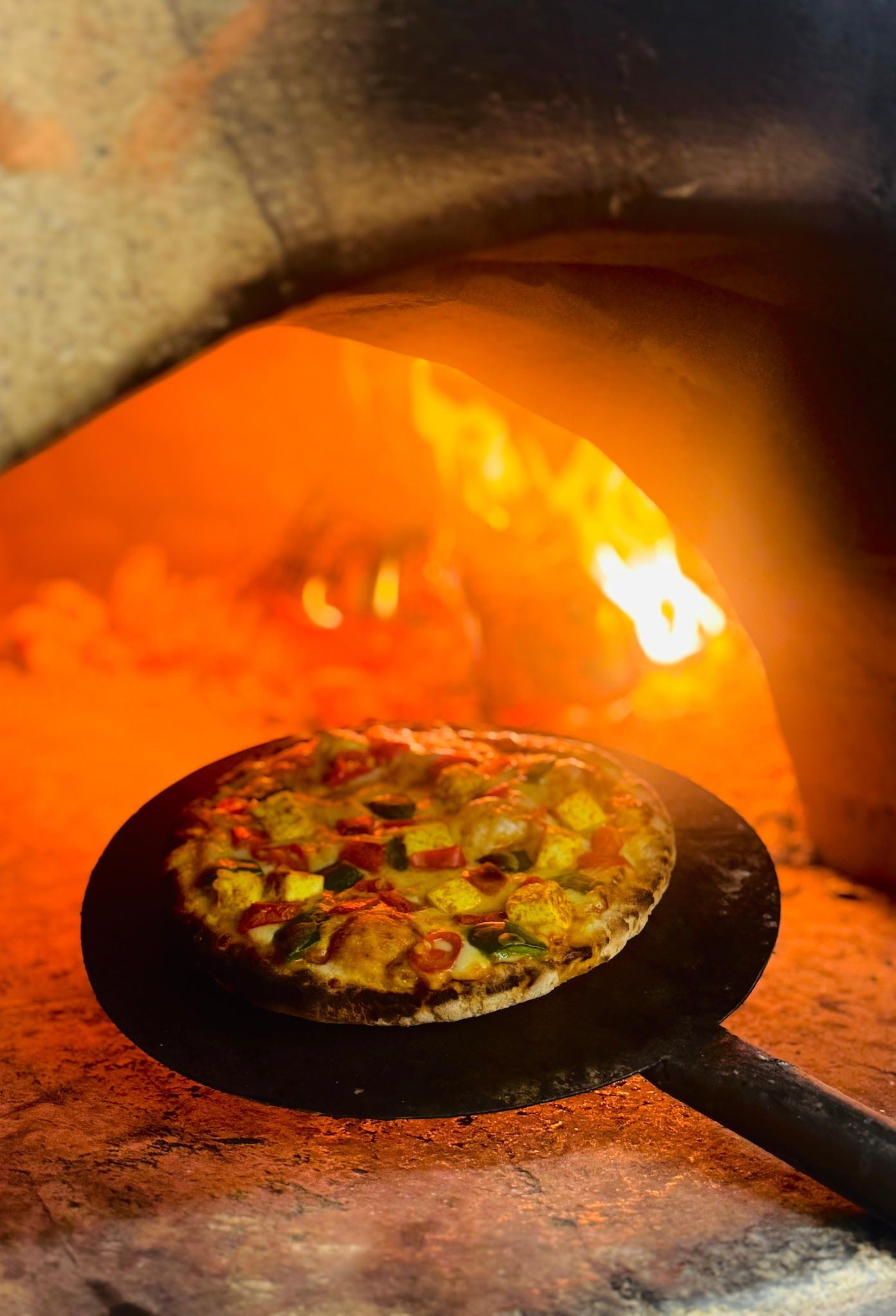 A vegetable pizza on a peel inside Veda’s blazing wood-fired oven