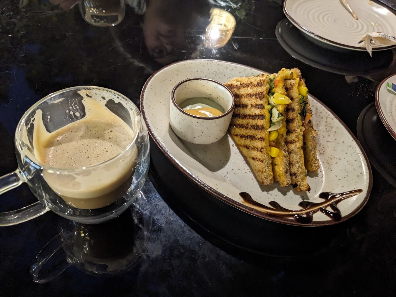 A grilled sandwich and a glass mug of coffee